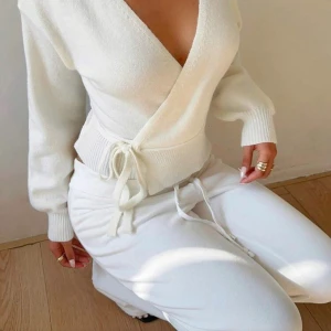 Vit omlottstickad kofta med knyt - ANVÄND EN GG! Superfin vit stickad kofta med omlottmodell och knyt i sidan. Tröjan har djup v-ringning, långa ärmar och bred ribbad mudd i midjan och vid ärmsluten. Perfekt att styla med jeans eller kjol för en clean look.