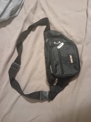 Svart axelväska från Seal Tech - Säljer en svart axelväska från Seal Tech med flera praktiska fack och dragkedjor. Väskan har justerbar rem och är tillverkad i slitstark syntet. Perfekt för att ha med sig det viktigaste och hålla koll på grejerna när du är på språng.