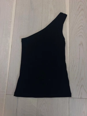 Svart oneshoulder topp från Kappahl - Säljer en svart ribbad oneshoulder topp från Kappahl i storlek XS. ❤️