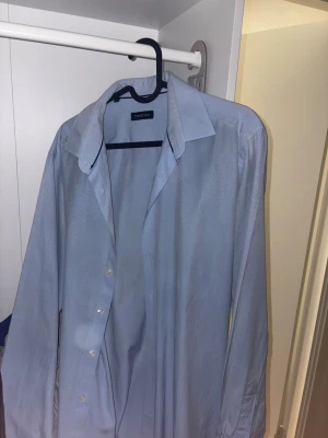 Ljusblå skjorta från Fabrika - Snygg ljusblå skjorta från Fabrika i storlek M. Skjortan har diskret mönster, klassisk krage och knappar framtill. Långärmad och tillverkad i mjukt bomullsmaterial som känns skönt mot huden. Perfekt för dig som gillar stilrena och enkla plagg.