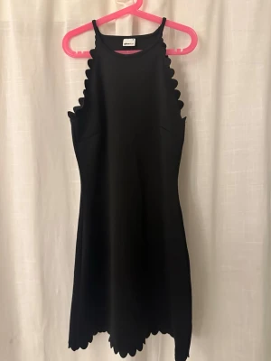 Svart klänning med scallop-detaljer - Svart klänning från Gina Tricot i storlek S. Modellen är ärmlös med scallop-detaljer längs kanterna och nederdelen. Klänningen har en rak passform och är kort i längden, perfekt för dig som gillar stilrena och moderna plagg.