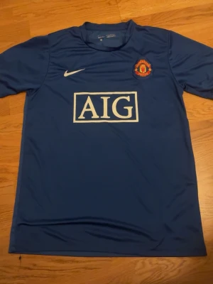 Man utd - Bilden visar ingen sko, utan en blå Manchester United-tröja från Nike med AIG-logga på bröstet.