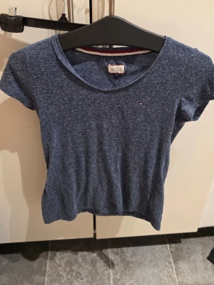 Blå t-shirt från Tommy Hilfiger - Säljer en blåmelerad t-shirt från Tommy Hilfiger Denim i storlek S. Toppen har rund halsringning, korta ärmar och en liten broderad logga på bröstet. Materialet är en mix av bomull och polyester vilket gör den mjuk och skön.