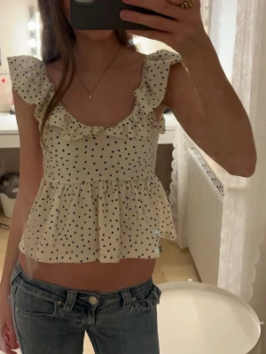 Prickig volangblus med öppen rygg  - Supersöt vit blus med svarta prickar och volangdetaljer vid axlarna, med öppen rygg. Säljer toppen för att den har blivit för kort för mig❣️