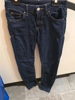 Mörkblå skinny jeans, storlek 34 - Snygga mörkblå skinny jeans i storlek 34 med klassisk femficksdesign och kontrastsömmar. Jeansen har normal passform och är tillverkade i mjukt jeansmaterial. Perfekta för dig som gillar en smal siluett och enkel stil.