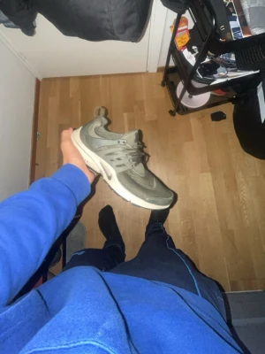 Nike Presto sneakers i olivgrönt - Nike Presto sneakers i olivgrönt med mesh-överdel och syntetdetaljer. Skon har snörning, rund tå och en beige platt sula med svart undersida. Snygg och sportig design med diskret Nike-logga på sidan. Perfekt för dig som gillar streetwear och bekväma skor.