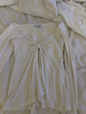  Design By Si tröja  - Säljer en beige omlottopp från Design By Si  i storlek XS/S. Toppen har lång ärm, v-ringad hals och snygg knytning framtill som ger en cool detalj. Materialet känns mjukt och har ett fint fall. Perfekt att styla med jeans eller kjol. Finns litet hål men de syns inte alls och går lätt att sy !