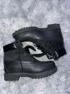 Svarta Timberland boots med snörning - Säljer ett par svarta Timberland boots med grov sula och snörning. Skorna har en kombination av mocka och skinn på ovandelen samt rund tå. Perfekta för dig som gillar robust stil och vill ha något som sticker ut lite extra.