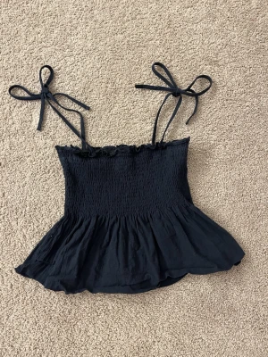 Marinblå topp med axelband - Fin marinblå topp med axelband. Axelbanden går själv att knyta och justera. Fin och perfekt att ha en varm sommardag. Strl XS