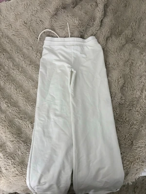 Vita vida mjukisbyxor med snörning - Säljer ett par vita mjukisbyxor med breda ben och dragsko i midjan. Byxorna har en relaxed fit och är tillverkade i mjukt bomullsmaterial. Perfekta för chill dagar eller när du vill ha det extra bekvämt.