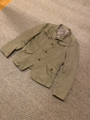 Olivgrön overshirt - Säljer en fet olivgrön kostym overshirt i nytt skick. Hittar inte någon lapp men skulle säga att den passar någon som har S-M. Vet ej märket på den. Skriv för fler frågor.