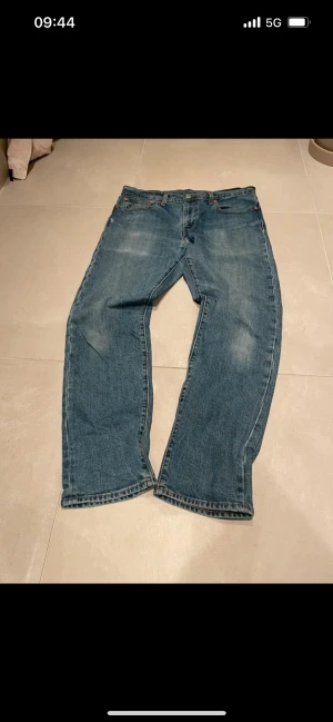 Levi's 502 blå jeans W33 L32 - Klassiska blå Levi's 502 jeans med rak passform och normal midja. Jeansen har fem fickor, snygga slitningar och den ikoniska läderpatchen bak i midjan. Perfekta för dig som gillar en tidlös och avslappnad stil.