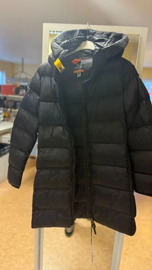 Svart lång dunjacka Parajumpers S - Säljer en svart lång dunjacka från Parajumpers med huva och dragkedja. Jackan har den klassiska gula detaljen vid halsen och är quiltad för extra värme. Perfekt för kalla dagar och riktigt snygg till vintern.