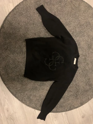 Svart stickad tröja från Guess  - Svart stickad tröja från Guess i storlek XS med stor, glittrig Guess-logga framtill. Tröjan har rund hals och långa ärmar, perfekt för dig som gillar stilrena och snygga plagg med en touch av branding. Materialet är mjukt och skönt och är lite tungt, vilket känns lyxigt. Nypris är någonstans över 1000 lappen, Inga defekter och i väldigt fint skick. Hör av dig vid frågor, pris går att diskutera💕