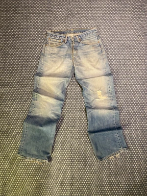Levis Vintage Jeans - Ljusblå Levis jeans med klassisk femficksdesign, slitningar och hål på ena knät samt fransiga benslut. Jeansen har rak passform och är tillverkade i bomull. Perfekt för dig som gillar en avslappnad och vintage look. Rinktigt vintage och med väldigt bra kavitet. Har en straight fit men är lite lite mer bredare, precis som man vill ha dem🙌 Om du undrar något är det bara att skriva✅