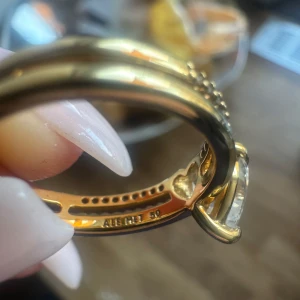 Pandora double heart ring  - Superfin guldring från Pandora  i storlek 50 med en stor hjärtformad klar sten i mitten och små gnistrande stenar längs bandet. Ringen har en elegant och romantisk design med guldfärgat band och levereras i en söt rosa ask.