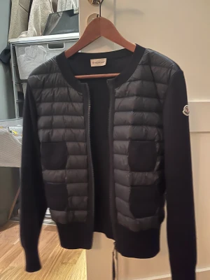 Svart quiltad pufferjacka från Moncler - Säljer en mörkblå/svart pufferjacka/cardigan från Moncler. Köpte den ny vintern 2023. Den är inte alls använd (skulle till och med säga nyskick).  Storlek M i den, men passar mindre men också större. Den är köpt  i den mörkblå färgen 