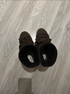 Bruna Inuikii boots med snörning - Säljer ett par bruna boots från Inuikis. Skorna har en platt sula och är fodrade med mjukt material på insidan för extra värme. Utsidan är i mocka och skinn, perfekt för kyliga dagar. Snygg och chunky look som passar till streetwear.