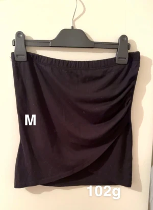 Svart kortkjol, storlek M - En enkel svart kortkjol med elastisk midja. Kjolen har en lätt omlott-effekt framtill som ger en snygg drapering. Perfekt att matcha med en crop top eller hoodie för en chill look.🌸Fint använt skick. Storlek M