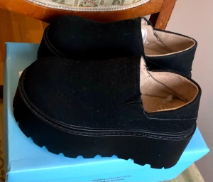 Svarta plattformsskor med grov sula - Säljer ett par svarta slip-on skor med rejäl plattformssula och rund tå. Ovandelen är i textil och insidan är ljusbeige. Skorna har en chunky look och passar dig som gillar att sticka ut med din stil.