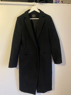 Svart kappa från Crocker - Stilren svart kappa från Crocker i storlek S. Sitter mer figursydd än vad det set ut, modell med krage och två fickor framtill. Säljs pga storlek