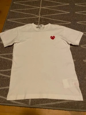 Vit Comme des Garçons Play t-shirt M - Säljer en clean vit t-shirt från Comme des Garçons Play i storlek M. T-shirten har ett ikoniskt rött hjärta med ögon broderat på bröstet. Klassisk rund hals och korta ärmar. Tillverkad i mjuk 100% bomull för skön känsla. Skicka 9/10 inte använd alls. Priset kan diskuteras 😀❤️🎉
