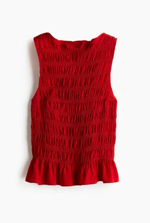 Röd smockad ärmlös topp - Säljer en röd ärmlös topp med smockad struktur och volangkant nedtill. 