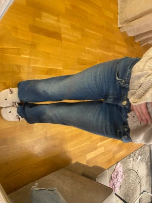 Blå bootcut jeans från 1974 - Snygga blå jeans från 1974 med bootcut passform och klassiska fickor med knappdetaljer bak. Jeansen har en mörk tvätt med lätt slitning vid benslut och midwaist. Perfekta för dig som gillar retrovibbar och bekväm stil.