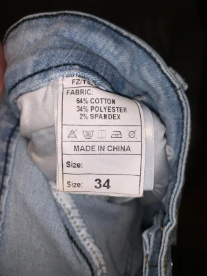 Ljusblå cargopants i jeans, storlek 34 - Säljer ett par ljusblå cargopants i jeansmaterial med slitna detaljer och stora fickor på benen. Byxorna har en cool tvättad look och är tillverkade av bomull, polyester och lite spandex för extra stretch. Perfekt för dig som gillar streetstyle och vill sticka ut.