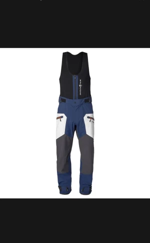 Sail Racing Seglarbyxor Gore-Tex  blå vit grå  - Nya Sail Racing Tuwok Bib Pants, tillverkade i 3-lagers GORE-TEX®-tyg med förböjda ben och förstärkningar vid knän och bak. Neopren i midjans insida och elastisk justering med kardborreknäppning på utsidan av midjan. Den övre delen är avtagbar, tillverkad i dubbel stretchig mesh med vattenavvisande dragkedja fram. En ficka på höger ben med vattenavvisande dragkedja och logo-broderi. Dem är helt nya, aldrig använda med lappar kvar. Pris kan diskuteras vid snabb affär. Skriv för fler bilder