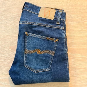 Nudie Jeans Grim Tim - Schyssta jeans från Nudie, modellen är grim Tim. Färg är indigo myth och de är W30 L30. De har en väldigt liten reva på höger knä men är i övrigt i suveränt skick! Hör av er vid minsta fundering!