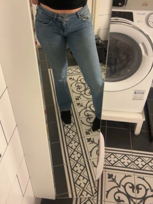 Blå låg midjade bootcut jeans med normal midja - Säljer ett par klassiska blå jeans med bootcut-snitt och normal midja. är tillverkade i ett mjukt denimtyg som sitter snyggt över höfterna och låren. Perfekt för dig som gillar en tidlös och chill stil.