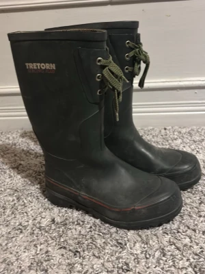 Svarta Tretorn stövlar med snörning - Säljer ett par svarta Tretorn Strong stövlar med gröna snören och grov sula. Stövlarna är tillverkade i slitstarkt gummi och har en diskret röd linje runt sulan. Insidan är ljus med Tretorn-logga. Perfekt för regniga dagar.