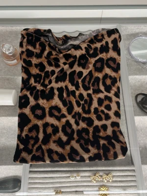 Leopardmönstrad ärmlös topp från Lager 157 S - Säljer en snygg ärmlös topp med leopardmönster i bruna och svarta toner från Lager 157. Toppen har en rak passform och är tillverkad i mjukt syntetmaterial som känns skönt mot huden. Perfekt att styla med jeans eller kjol för en cool look.