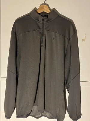Mörkgrå half zip tröja Callaway XL - Säljer en mörkgrå långärmad tröja från Callaway i storlek XL. Tröjan har en praktisk half zip framtill och är tillverkad i ett lätt och funktionellt syntetmaterial med Opti-Dri teknologi. Perfekt för träning eller golf och har en stilren design med diskret logga på bröstet.