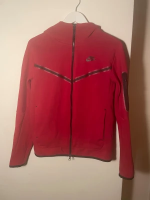 Röd Nike tech fleece (pris kan diskuteras) - Snygg Nike tech fleece. Säljer eftersom att jag växt ur den. Den är inte navänd så mycket och har inga synliga fläckar. Köpt i Nike affär.