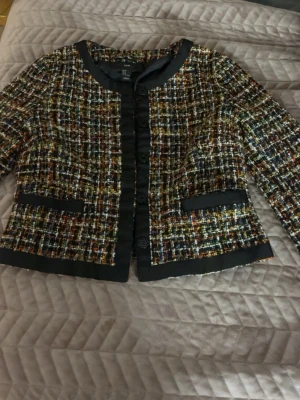 Rutig kavajjacka från H&M, strl 42 - Säljer en snygg rutig kavajjacka från H&M i storlek 42. Jackan har ett färgstarkt rutmönster med inslag av svart, orange, gul och blå, samt svarta detaljer och knappar framtill. Materialet är grovt och känns lyxigt, perfekt för att lyfta din outfit.