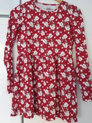 Klänning - Superfin röd klänning från Mywear Young med ett gulligt snögubbemönster över hela plagget. Klänningen har lång ärm och rund halsringning, perfekt för vinterns mysiga dagar. Tillverkad i mjuk bomull som är skön att ha på sig.
