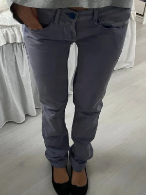 Lila raka byxor från Acne Studios - Säljer ett par lila byxor från Acne Studios med raka ben och klassisk femficksmodell. Byxorna har låg midja, diskreta sömmar och en enkel knappstängning framtill. Materialet är mjukt och har en lätt glansig finish som ger en clean look.