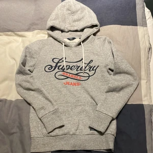 Superdry hoodie - Säljer en grå hoodie från superdry. Tröjan är i storlek xs men är ganska tajt så passar som xxs om man inte vill ha den lika tajt. Tröjan är i bra skick och har inga defekter. Hör av dig vid frågor😁