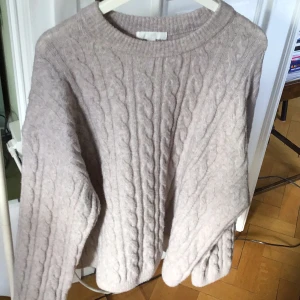Beige stickad tröja från H&M - Mysig beige stickad tröja från H&M med kabelstickat mönster. Perfekt för kyliga dagar med sin varma och bekväma design. Tröjan har långa ärmar och en rund halsringning. Ganska vid känns som strl M/L.