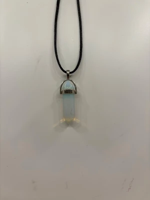 Opalit kristallhalsband med svart snöre - Säljer ett snyggt halsband med ett opalit kristallhänge i ljusblå och vita toner. Hänget har en metallfattning och hänger på ett svart justerbart snöre. Perfekt accessoar för dig som gillar kristaller och stilrena smycken. Köpt i Cypern🇨🇾