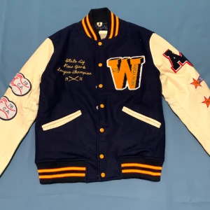 American College Varsity Jacket - Marinblå - Storlek M  Helt ny, har endast testat den.  Mjuk och varm jacka i klassisk college-stil.  Passform: Unisex. Säljes pga fel storlek. Perfekt skick – först till kvarn! Priset kan diskuteras.