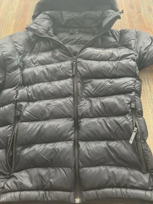 Svart dunjacka Peak Performance - Svart dunjacka från Peak Performance i storlek 170. Har tappat drag grenen från dragkedjan på höger fickan men annars i bra använt skick. Ny pris runt 2000kr.