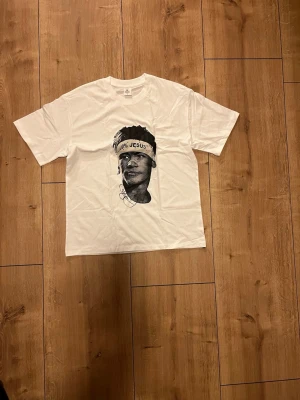 Vit t-shirt med grafiskt tryck, Neymar - Vit t-shirt med ett stort svartvitt grafiskt tryck av Neymar med texten '100% JESUS' på ett pannband me. Klassisk passform och rund hals. Perfekt för dig som gillar streetstyle.