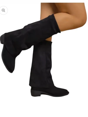 Svarta höga boots i mocka - Säljer ett par svarta boots med högt skaft och platt sula. Skorna har en rund tå och är tillverkade i mjuk mocka som ger en snygg och stilren look. Perfekta att matcha med jeans eller kjol för en cool vibe.