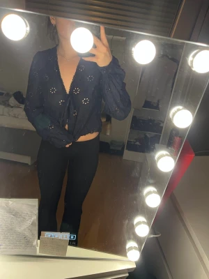 Blå blus med blomdetaljer - Blå blus i tunt linne tyg med knyt detaljer och knappar i mitten. Köpt från Nelly.