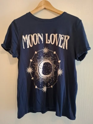 Blå Moon Lover t-shirt från FB Sister - Snygg mörkblå t-shirt från FB Sister med trycket 'Moon Lover' och ett coolt månmotiv på framsidan. Modellen är regular fit med korta ärmar och rund hals. Perfekt för dig som gillar unika prints och mjuk bomullskänsla.