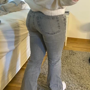 Low waist bootcut jeans - Snygga grå jeans från Gina Tricot med bootcut passform och låg midja. Jeansen har dubbla knappar fram, klassiska fickor och en cool fickdetalj med lock. Materialet är mjukt jeans-tyg som sitter bekvämt och ger en schysst siluett. Har defekter på ett lår (se sista bild) men inget som syns tydligt. Där av priset, orginalpris är 399💕 