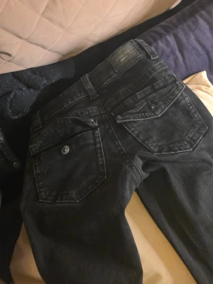 Svarta jeans från Perfect Jeans - Säljer ett par svarta jeans från Perfect Jeans med stora bakfickor som har lock och knapp. Jeansen har klassisk femficksdesign och är gjorda i ett mjukt jeansmaterial. Perfekt för dig som gillar en enkel och stilren look.